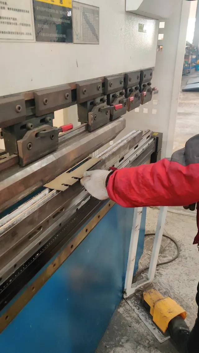 A worker bends a sheet-metal part using a press brake in a workshop.